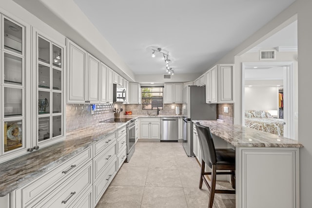 112 Piedmont C, Delray Beach, FL 33484 - kitchen featuring stainless steel appliances, tasteful backsplash, light stone countertops, light tile patterned floors, and a kitchen bar