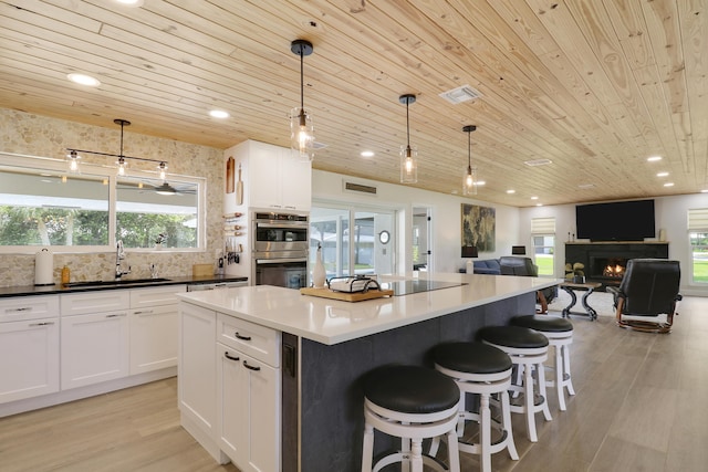 386 NE Ficus Ter, Jensen Beach, FL 34957 - kitchen with wood ceiling, a sink, white cabinetry, light wood-style flooring, and a lit fireplace