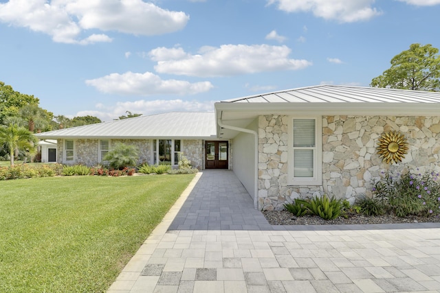 386 NE Ficus Ter, Jensen Beach, FL 34957 - ranch-style house featuring stone siding, a front yard, metal roof, a standing seam roof, and french doors