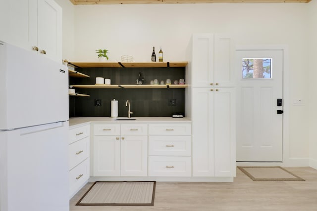386 NE Ficus Ter, Jensen Beach, FL 34957 - kitchen with freestanding refrigerator, light wood-type flooring, backsplash, white cabinetry, and a sink