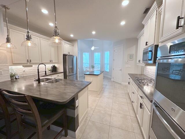 9624 SW Royal Poinciana Dr, Port Saint Lucie, FL 34987 - kitchen featuring stainless steel appliances, dark countertops, tasteful backsplash, a kitchen island, and a sink