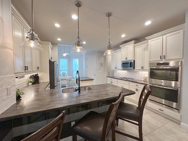 9624 SW Royal Poinciana Dr, Port Saint Lucie, FL 34987 - kitchen featuring appliances with stainless steel finishes, a sink, dark countertops, backsplash, and a peninsula