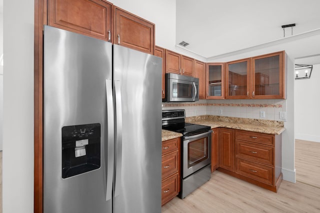 2707 SE Rawlings Rd, Port Saint Lucie, FL 34952 - kitchen featuring appliances with stainless steel finishes, brown cabinetry, light wood-style flooring, backsplash, and light stone counters