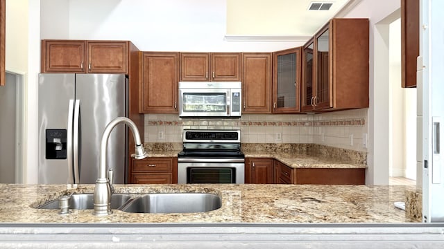 2707 SE Rawlings Rd, Port Saint Lucie, FL 34952 - kitchen featuring stainless steel appliances, brown cabinetry, a sink, and tasteful backsplash