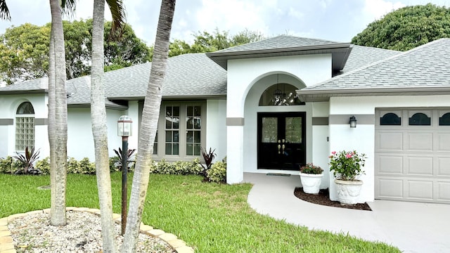 2707 SE Rawlings Rd, Port Saint Lucie, FL 34952 - doorway to property featuring roof with shingles, stucco siding, a garage, a lawn, and french doors