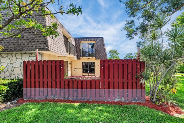 2883 SW 22nd Cir E Unit 51A, Delray Beach, FL 33445 - view of side of property with a balcony, mansard roof, a fenced front yard, roof with shingles, and stucco siding