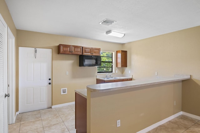 1332 SW G, Belle Glade, FL 33430 - kitchen featuring black microwave, a peninsula, light countertops, baseboards, and brown cabinetry