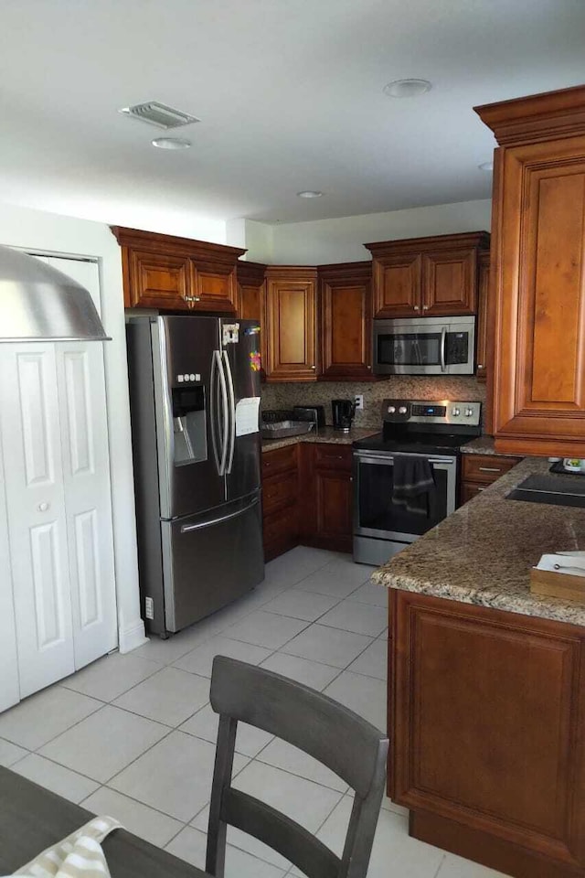4097 Bluff Harbor Way, Wellington, FL 33449 - kitchen with appliances with stainless steel finishes, tasteful backsplash, light tile patterned flooring, dark stone counters, and brown cabinetry