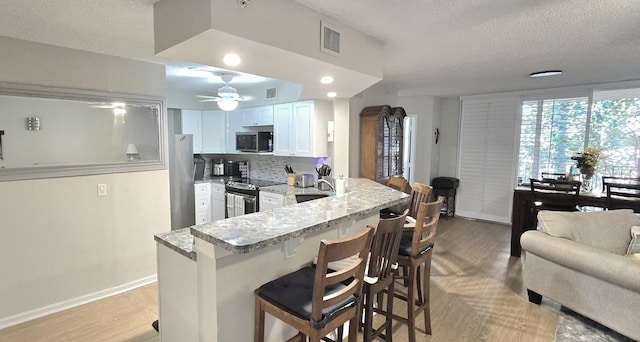 700 Scotia Dr Unit 202, Hypoluxo, FL 33462 - kitchen with stainless steel appliances, a breakfast bar, light wood-style floors, a peninsula, and a textured ceiling