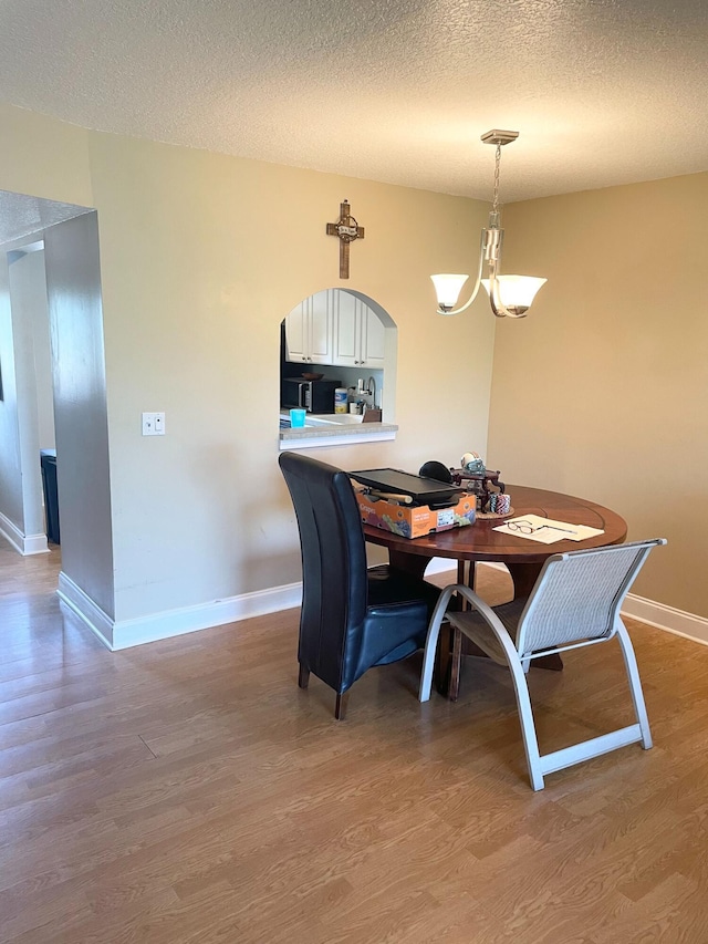 829 Camino Rd Unit 206-C, Delray Beach, FL 33445 - dining space featuring a chandelier, light wood-style flooring, baseboards, a textured ceiling, and arched walkways