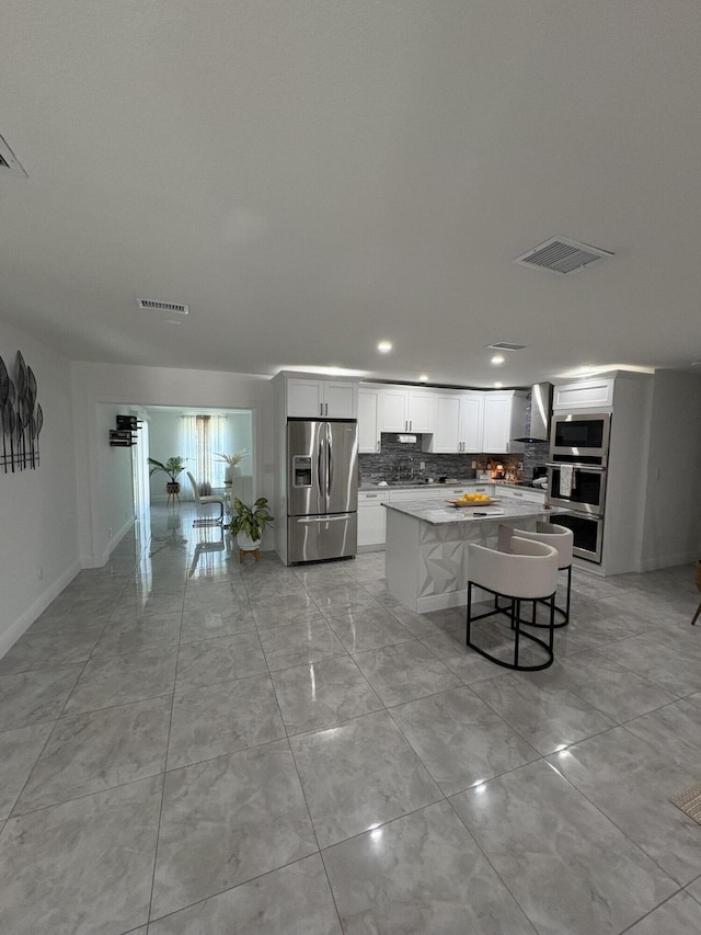 305 E 6th St, Lehigh Acres, FL 33972 - kitchen with stainless steel appliances, wall chimney exhaust hood, a kitchen island, decorative backsplash, and white cabinets