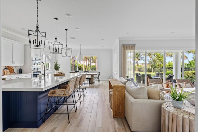 12277 Waterstone Cir, Palm Beach Gardens, FL 33412 - kitchen featuring open floor plan, light countertops, a chandelier, crown molding, and light wood finished floors