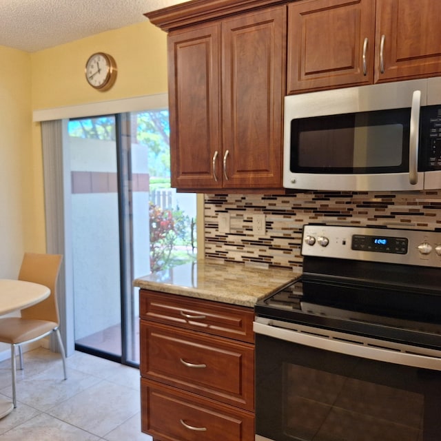 10231 N Circle Lake Dr Unit 101, Boynton Beach, FL 33437 - kitchen with appliances with stainless steel finishes, backsplash, light stone countertops, light tile patterned flooring, and a textured ceiling