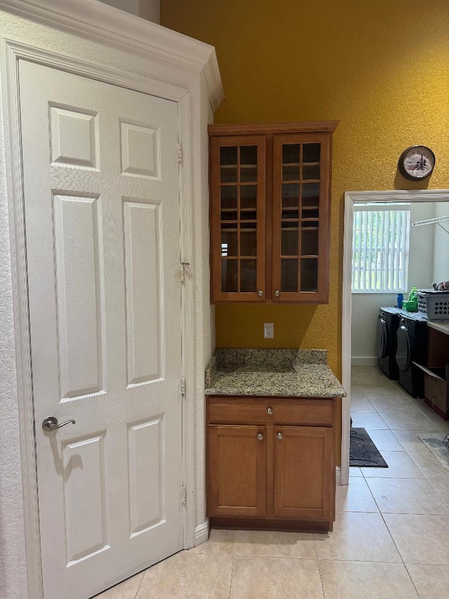 5760 NW Cleburn Dr, Port Saint Lucie, FL 34986 - kitchen with glass insert cabinets, washer / clothes dryer, light tile patterned floors, and brown cabinetry