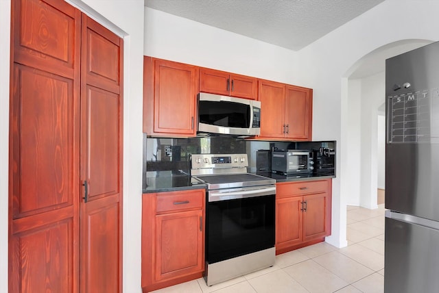 3769 Pebblebrook Ct, Coconut Creek, FL 33073 - kitchen featuring stainless steel appliances, dark countertops, backsplash, arched walkways, and light tile patterned floors