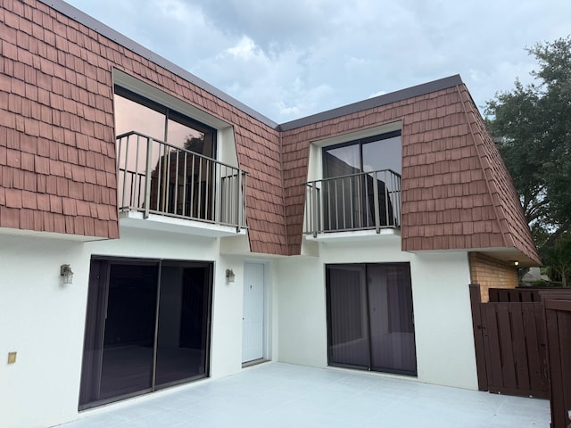 3611 SW Sunset Trace Cir, Palm City, FL 34990 - back of house with mansard roof, stucco siding, a patio area, and a balcony