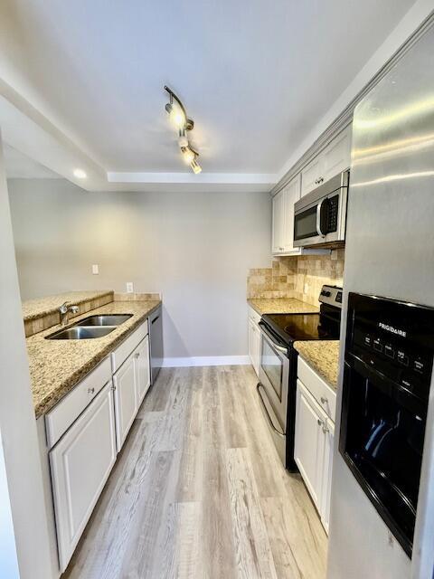 3611 SW Sunset Trace Cir, Palm City, FL 34990 - kitchen with appliances with stainless steel finishes, a sink, light wood-type flooring, tasteful backsplash, and white cabinetry