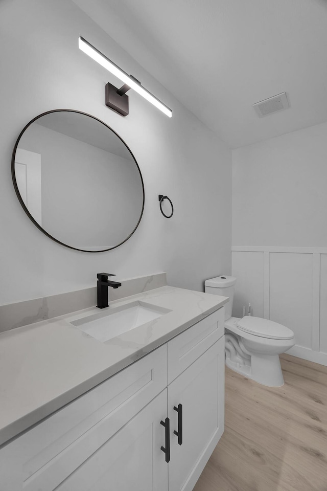 2033 SW Justison Ave, Port Saint Lucie, FL 34953 - bathroom featuring wood finished floors, vanity, toilet, wainscoting, and a decorative wall