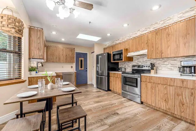 2550 SE Calais St, Port Saint Lucie, FL 34952 - kitchen with stainless steel appliances, under cabinet range hood, light countertops, light wood-style floors, and decorative backsplash