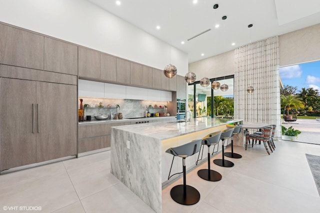 8533 N Native Dancer Rd, Palm Beach Gardens, FL 33418 - kitchen with a sink, modern cabinets, light stone counters, backsplash, and a breakfast bar