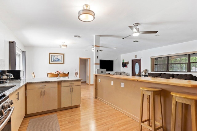 1045 NW 47th Ter, Miami, FL 33127 - kitchen featuring stainless steel range, light wood-style floors, ceiling fan, and a kitchen bar