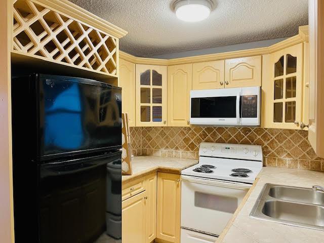 4491 NW 1st Ter, Deerfield Beach, FL 33064 - kitchen with white appliances, light countertops, glass insert cabinets, a sink, and a textured ceiling