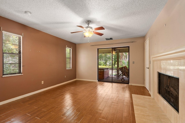 4904 River Pl, Fort Pierce, FL 34982 - unfurnished living room with a tiled fireplace, a textured ceiling, baseboards, a ceiling fan, and wood finished floors