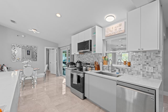 2471 SE Leithgow St, Port Saint Lucie, FL 34952 - kitchen with stainless steel appliances, a sink, decorative backsplash, vaulted ceiling, and white cabinets