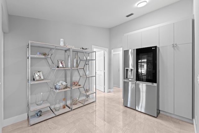 2471 SE Leithgow St, Port Saint Lucie, FL 34952 - kitchen with stainless steel fridge, white cabinetry, baseboards, and light marble finish floors