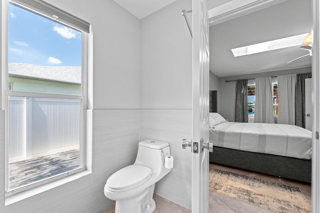 2471 SE Leithgow St, Port Saint Lucie, FL 34952 - bathroom featuring ensuite bath, a skylight, toilet, tile walls, and a wainscoted wall