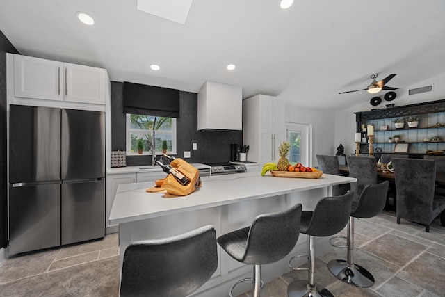 14244 Horseshoe Trce, Wellington, FL 33414 - kitchen featuring freestanding refrigerator, white cabinetry, a breakfast bar area, light countertops, and stone tile floors