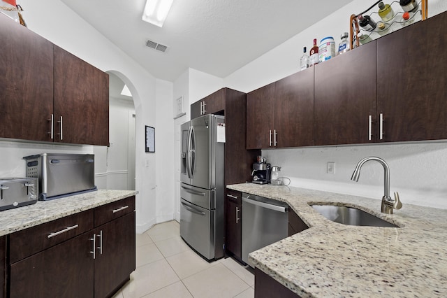 899 Pipers Cay Dr, West Palm Beach, FL 33415 - kitchen with appliances with stainless steel finishes, a sink, light stone countertops, light tile patterned floors, and arched walkways