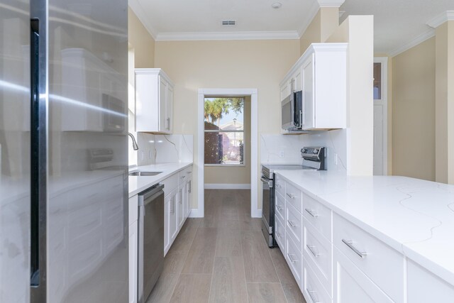 2608 SW Greenwich Way, Palm City, FL 34990 - kitchen featuring stainless steel appliances, white cabinetry, decorative backsplash, crown molding, and light stone counters