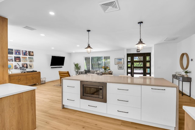 354 Country Club Dr, Tequesta, FL 33469 - kitchen with stainless steel microwave, white cabinetry, modern cabinets, decorative light fixtures, and light wood-style floors