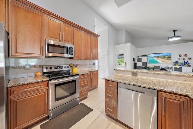 13595 89th Pl N, West Palm Beach, FL 33412 - kitchen featuring appliances with stainless steel finishes, vaulted ceiling, brown cabinetry, decorative backsplash, and light stone countertops