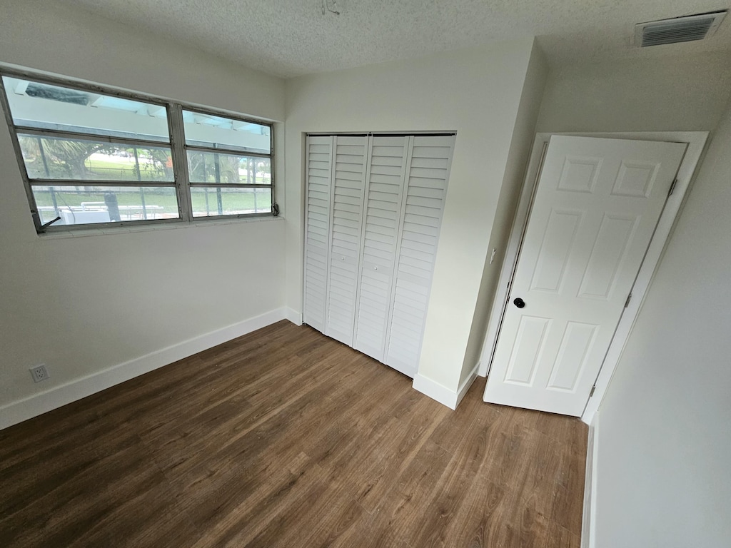 99 Henthorne Dr, Palm Springs, FL 33461 - unfurnished bedroom featuring dark wood-style floors, a textured ceiling, a closet, and baseboards