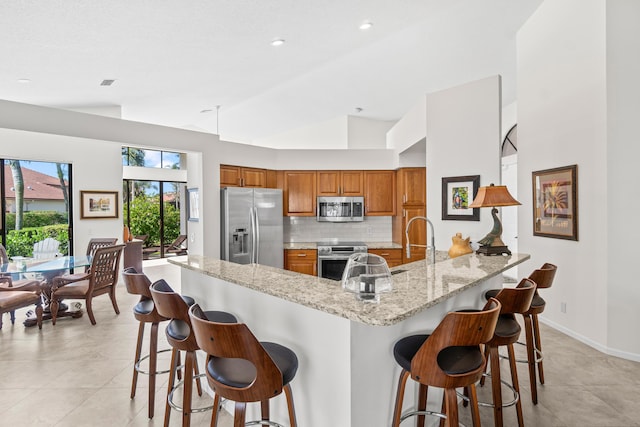 10194 N Lexington Cir, Boynton Beach, FL 33436 - kitchen with stainless steel appliances, brown cabinets, lofted ceiling, a peninsula, and light stone counters