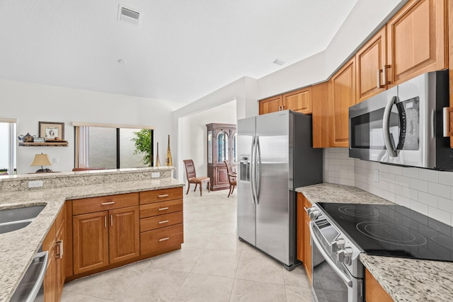 10194 N Lexington Cir, Boynton Beach, FL 33436 - kitchen featuring appliances with stainless steel finishes, backsplash, brown cabinets, light stone countertops, and light tile patterned floors