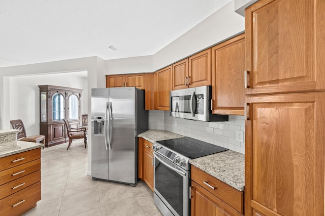 10194 N Lexington Cir, Boynton Beach, FL 33436 - kitchen with stainless steel appliances, decorative backsplash, brown cabinets, light stone countertops, and light tile patterned floors