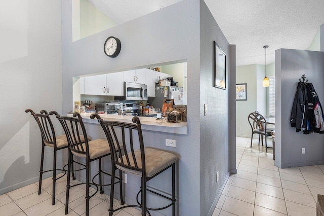 15318 W Tranquility Lake Dr, Delray Beach, FL 33446 - kitchen featuring appliances with stainless steel finishes, white cabinetry, light tile patterned floors, a kitchen breakfast bar, and baseboards