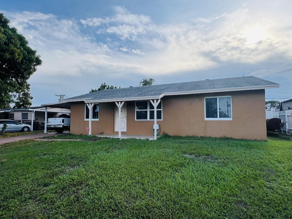 857 Scott Dr, West Palm Beach, FL 33415 - ranch-style house featuring stucco siding, a carport, a front lawn, driveway, and a shingled roof