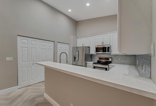 8592 Logia Cir, Boynton Beach, FL 33472 - kitchen with appliances with stainless steel finishes, a high ceiling, backsplash, white cabinetry, and a peninsula