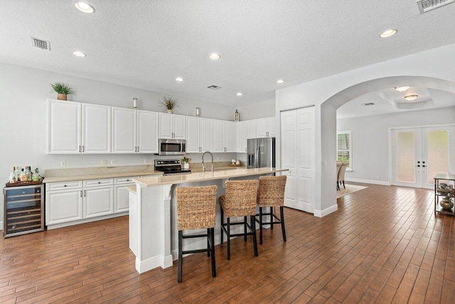 8940 New Hope Ct, West Palm Beach, FL 33411 - kitchen featuring appliances with stainless steel finishes, beverage cooler, arched walkways, a kitchen bar, and light countertops