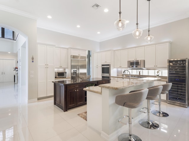 8784 Lewis River Rd, Delray Beach, FL 33446 - kitchen featuring beverage cooler, stainless steel appliances, a kitchen island with sink, arched walkways, and crown molding