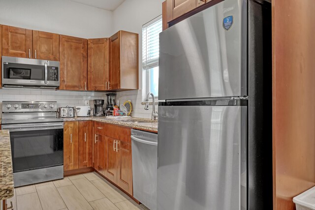 309 NE 11th Ave, Boynton Beach, FL 33435 - kitchen featuring appliances with stainless steel finishes, a sink, tasteful backsplash, light stone counters, and brown cabinetry