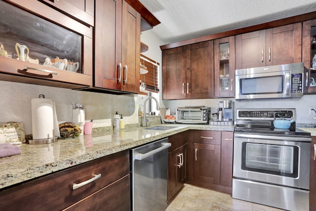 2850 Carambola Cir S Unit 19121, Coconut Creek, FL 33066 - kitchen with stainless steel appliances, a sink, light stone countertops, glass insert cabinets, and dark brown cabinets