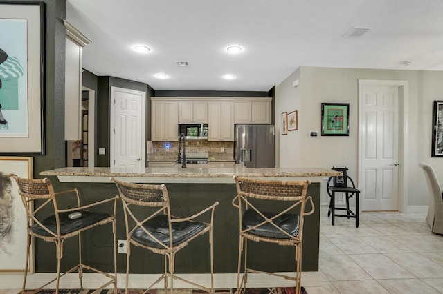 4884 SW Gossamer Cir, Palm City, FL 34990 - kitchen with appliances with stainless steel finishes, a breakfast bar area, backsplash, light stone countertops, and cream cabinetry
