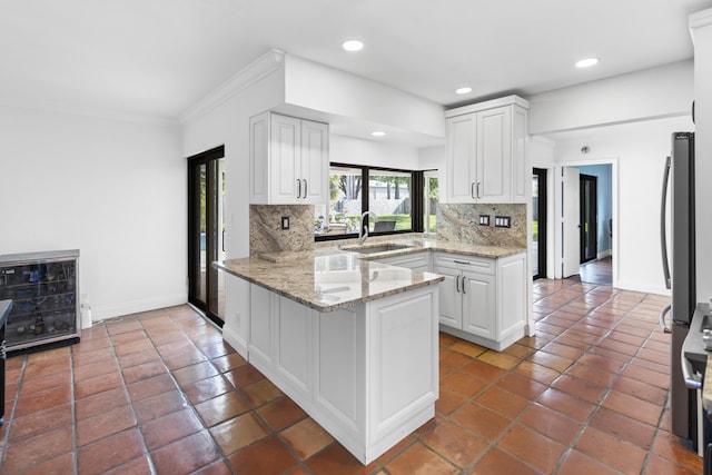 1318 NW 4th St, Boca Raton, FL 33486 - kitchen with a peninsula, backsplash, white cabinetry, ornamental molding, and light stone counters