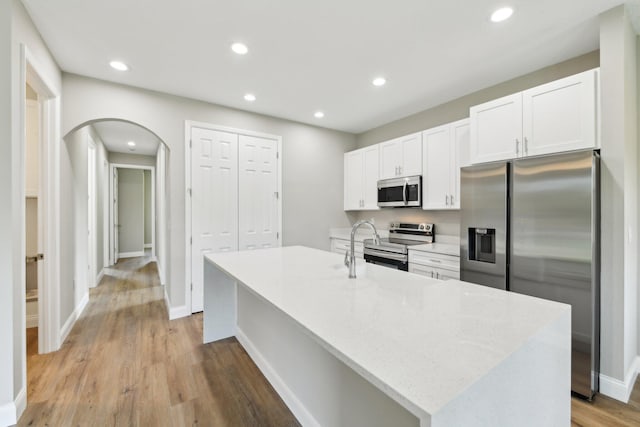 518 Scodella St SW, Palm Bay, FL 32908 - kitchen featuring stainless steel appliances, arched walkways, white cabinets, a kitchen island with sink, and light wood-style flooring