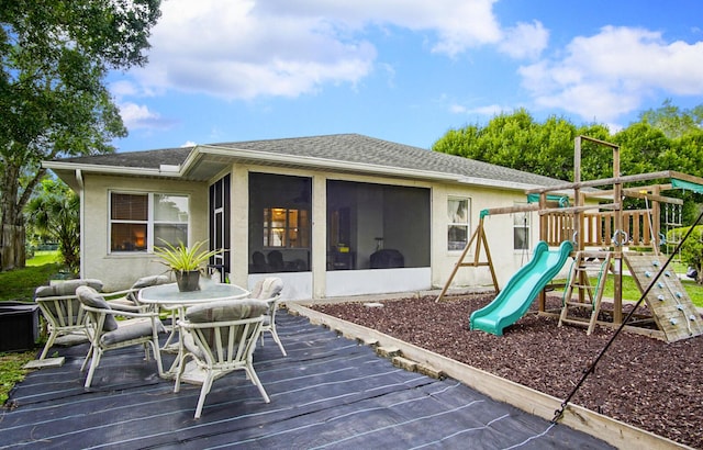 697 SW Dairy Rd, Port Saint Lucie, FL 34953 - rear view of property featuring a playground, a sunroom, a deck, a shingled roof, and stucco siding